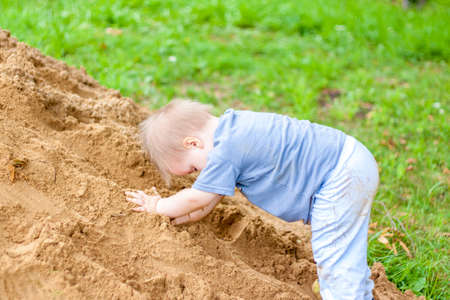 A little boy climbs a mountain with sand. The child is all dirty, but happy. Summer.の写真素材