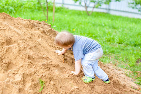A little boy climbs a mountain with sand. The child is all dirty, but happy. Summer.の写真素材