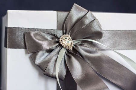 The gift box is white with a beautiful gray bow. Gift on a dark background. Holidays and surprises. Satin bows with rhinestones.の写真素材