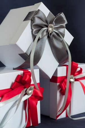 Many gifts. The gift box is white with a red and gray beautiful bow. Gift on a dark background. Holidays and surprises. Satin bows with rhinestones.の写真素材