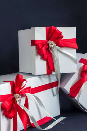 The gift box is white with a beautiful red bow. Gift on a dark background. Holidays and surprises. Satin bows with rhinestones.の写真素材