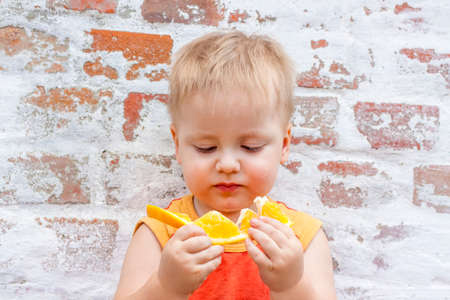 Portrait of child. Cute boy posing with an orange. The emotions of a child. Portrait of a boy against a brick wall.の写真素材