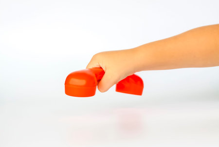 Red toy phone in the child's hand. Close-up of a child's hand. Isolated on a white background. The...