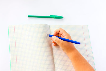 The child holds his hands over an open notebook and is going to write in it. Close-up of a child's...
