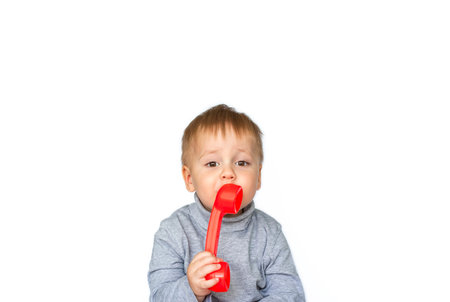 Portrait of a surprised cute little boy holding a red telephone receiver. The child is isolated on a...