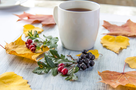 Autumn background with a Cup of tea, berries and yellow leaves on a painted wooden surface. Autumn...