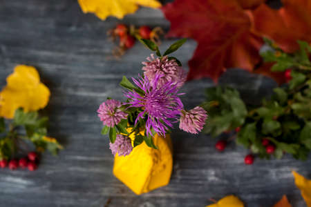 A bouquet of purple flowers in a yellow vase on a dark background. Autumn composition with flowers.の写真素材