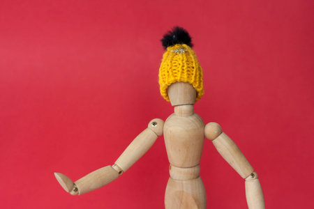 A wooden mannequin of a man in a knitted yellow hat points to a place next to him. Mannequin of a...