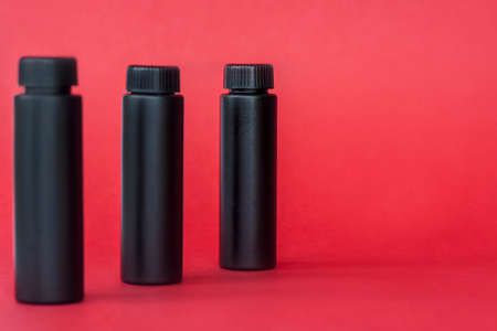 Black bottles with cream on a red background. Skin care, Moisturizing and nourishing or sunscreen. Industry of cosmetic beauty products.の写真素材