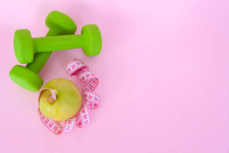 A green apple, and a centimeter measuring tape on a pink background. Sports, sports nutrition, healthy eating, diet. Space for the text. Exercise, lose weightの写真素材