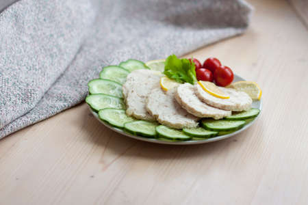 Cut the meat of a baked chicken into slices. Slices of baked chicken meat are laid out on a plate along with cucumber and cherry tomatoes. Homemade chicken sausage.の写真素材