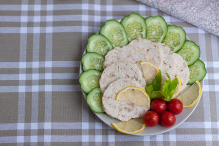 Cut the meat of a baked chicken into slices. Slices of baked chicken meat are laid out on a plate along with cucumber and cherry tomatoes. Homemade chicken sausage.の写真素材
