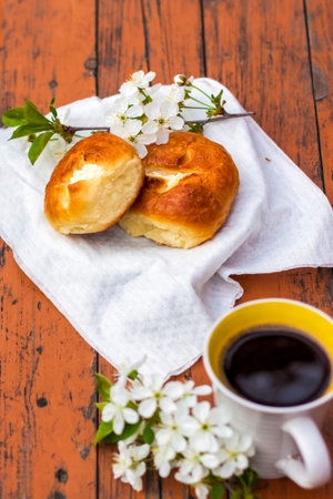 Baked open rolls and a cup of coffee on a dark, worn rustic wooden table. The composition is...