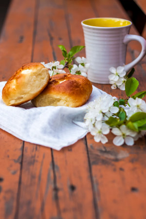 Baked open rolls and a cup of coffee on a dark, worn rustic wooden table. The composition is decorated with a twig with white flowers. Cherry tree flowers. Selective focus. Blurred background.の写真素材