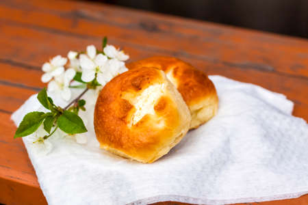 Baked open rolls on a dark, worn rustic wooden table. The composition is decorated with a twig with white flowers. Cherry tree flowers. Selective focus. Blurred backgroundの写真素材