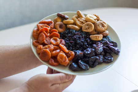 Men's hands hold a plate of dried fruit over the table. Prunes, dried apricots, figs, raisins on a large platter. Diet and the concept of beauty.の写真素材