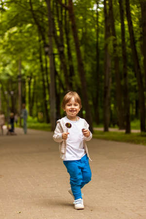 Cute little boy holding a large round lollipop on a stick. Joyful emotions. Sweets for small children. Summer outdoor activities. Preschooler with sugar candy. Children have a snack in the park.の写真素材