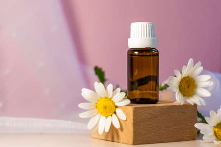 Bottle without label with oil on the stand. Transparent glass container with a dispenser on a beige-pink background. Product banner. Space for text, design. Cosmetology and the concept of beautyの写真素材