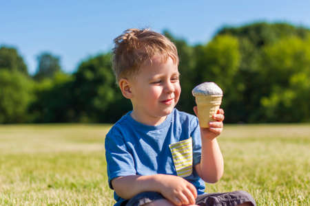 A happy boy is eating ice cream outdoors in the park. Refresh yourself with a cool ice cream on a hot day.の写真素材