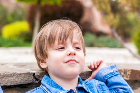 Close-up portrait of a small child smiling outdoors on a green background. Emotional child, joy, the concept of childhoodの写真素材