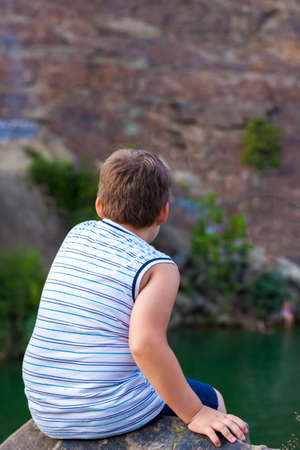 A child sits on the top of a beautiful canyon and looks at the water in it. The bank of the canyon. Portrait of a child.の写真素材