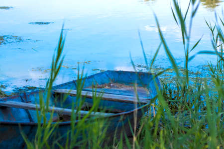 An old iron boat by the river. Reeds on the river under the sun. summer landscape with boats, close-up on the backgroundの写真素材