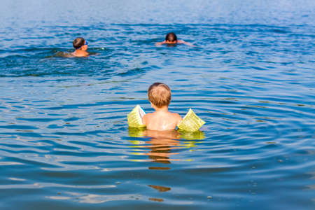 A family, a father and his sons are swimming in the river on a very hot summer day. Swim in reservoirs. A happy family has fun and splashes in the water in the summer. Family on vacationの写真素材