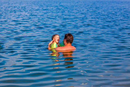 A family, a father and his sons are swimming in the river on a very hot summer day. Swim in reservoirs. A happy family has fun and splashes in the water in the summer. Family on vacationの写真素材