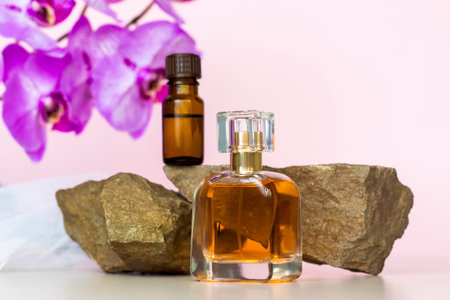 A cosmetic product and a perfume bottle stand on a stone against a background of beautiful orchids....