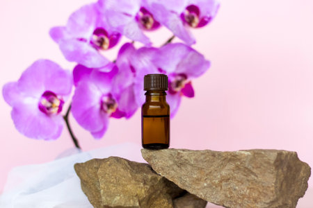 A brown bottle of cosmetic oil stands on a large structural stone with beautiful orchids next to it. Stylish appearance of the product, layout, personality. Banner, a place for the text.の写真素材