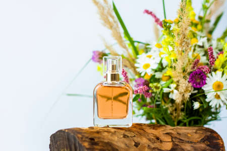 a perfume bottle on the background of a dry stump, tree bark and a bouquet of wild flowers. Stylish appearance, layout, personality. Banner, a place for the text. Background for advertising and presentation.の写真素材