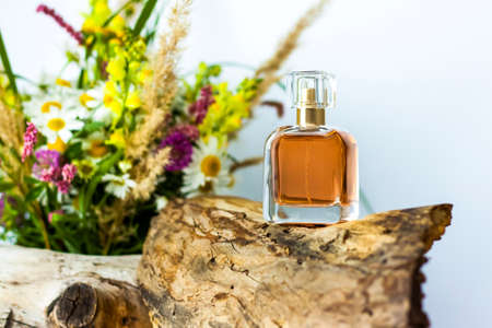a perfume bottle on the background of a dry stump, tree bark and a bouquet of wild flowers. Stylish appearance, layout, personality. Banner, a place for the text. Background for advertising and presentation.の写真素材