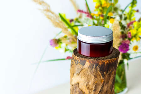 a jar of cream on the background of a dry stump, tree bark and a bouquet of wild flowers. Stylish appearance, layout, personality. Banner, a place for the text. Background for advertising and presentation.の写真素材