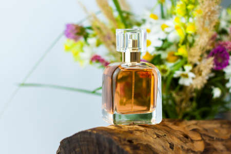 a perfume bottle on the background of a dry stump, tree bark and a bouquet of wild flowers. Stylish appearance, layout, personality. Banner, a place for the text. Background for advertising and presentation.の写真素材