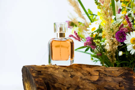 a perfume bottle on the background of a dry stump, tree bark and a bouquet of wild flowers. Stylish appearance, layout, personality. Banner, a place for the text. Background for advertising and presentation.の写真素材