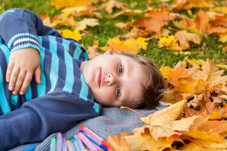 Autumn mood. The boy is thoughtfully drawing something in his notebook. Autumn portrait of a child in yellow foliage. Sight. A sweet, caring boy. Autumnの写真素材
