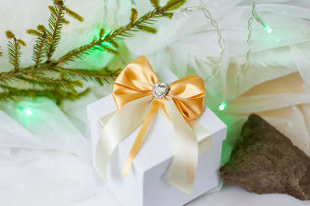 A Christmas gift decorated with a beautiful bow on a light background with a twig, if. Selective focus. the concept of Christmas and New Year. background for the banner.の写真素材