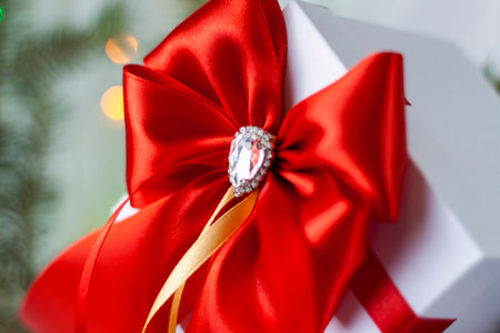 A Christmas gift decorated with a beautiful bow on a light background with a fir twig. Gifts, joy,...