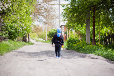 Wander alone along a rural street. A little boy is walking through the countryside. walk, view from the backの写真素材