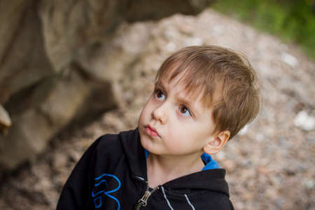 A boy-child on the background of a rocky mountain looks at something with curiosity and is surprised. Nature, rocks, mountains. Portrait of a cute boy outdoors.の写真素材