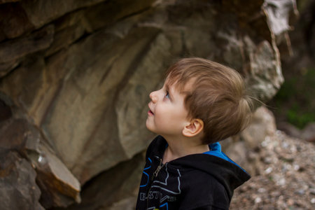 A boy-child on the background of a rocky mountain looks at something with curiosity and is...