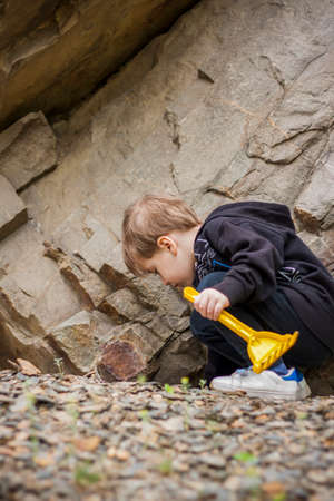 A boy-child on the background of a rocky mountain looks at something with curiosity and is surprised. Nature, rocks, mountains. Portrait of a cute boy outdoors.の写真素材
