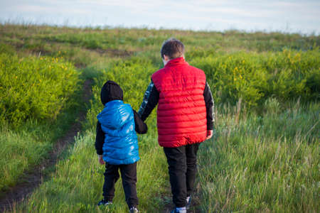 Children in the open spaces of the field are walking among the juicy spring grass in the light of sunset along a narrow trampled path. Landscape, countryside, springの写真素材