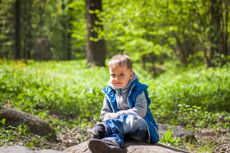 Portrait of a boy in a blue tank top in the woods in spring. Take a walk in the green park in the fresh air. The magical light from the sun's rays falls behind the boy. Springの写真素材
