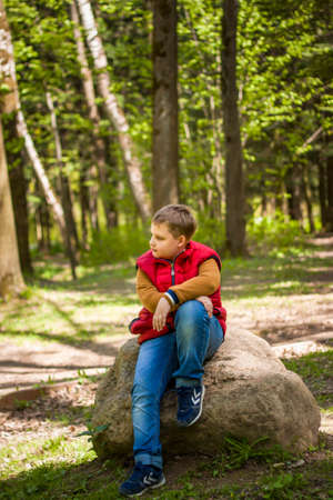 Portrait of a young man in a red tank top in the forest in spring. Walk through the green park in the fresh air. The magical light from the sun's rays falls behind the boy. Springの写真素材