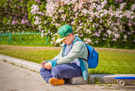 A young man is sitting on the side of a lilac alley and looking at his phone. Against the background of lilac bushes. interactions. selective focus. Springの写真素材