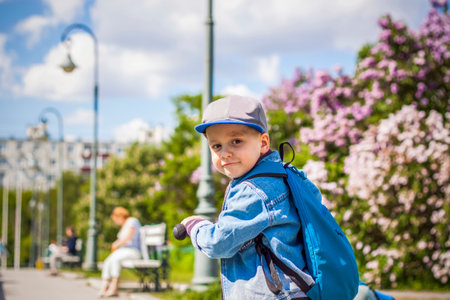 A boy in a baseball cap rides a scooter along a lilac alley . Against the background of lilac bushes. interactions. selective focus. Springの写真素材