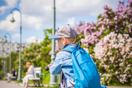 A boy with a blue backpack and a cap walks in the park.の写真素材