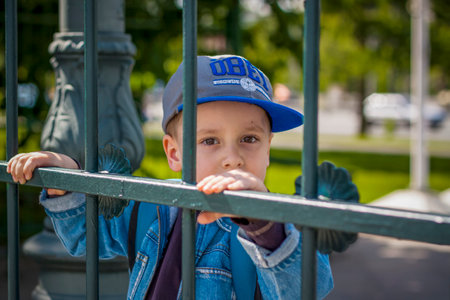 A boy in a cap and a blue jacket looks out of the fenceの写真素材