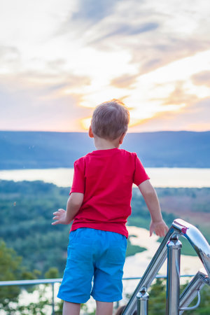 Cute Boy in a red T-shirt on the background of a stunning sunset. Journey. The face expresses natural joyful emotions. Not staged photos from nature.の写真素材
